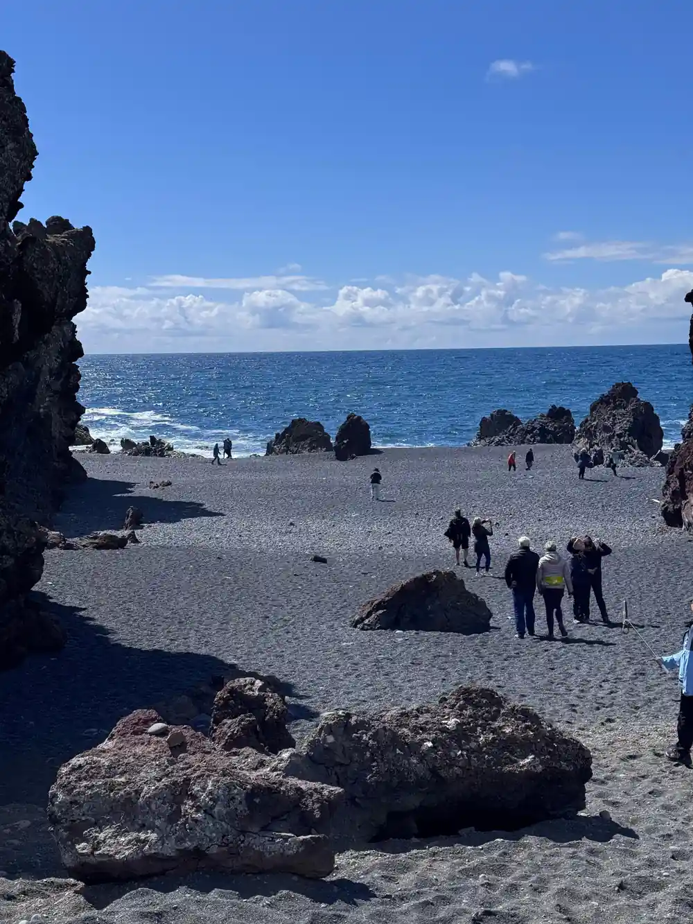 Beach with black sand, rocky outcrops and tourists gathered