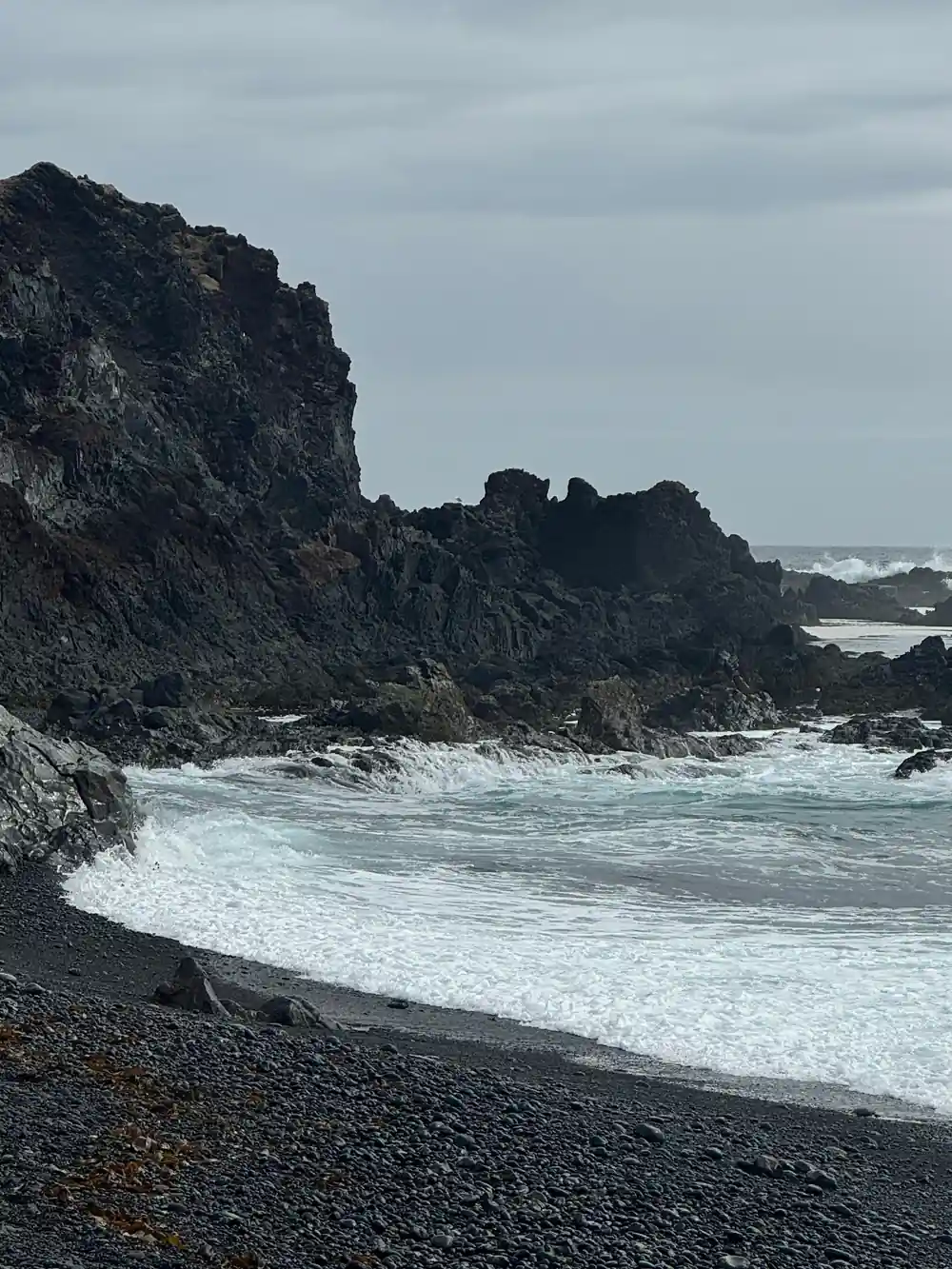 Black sand beach with rocky outcrop and turquoise waves
