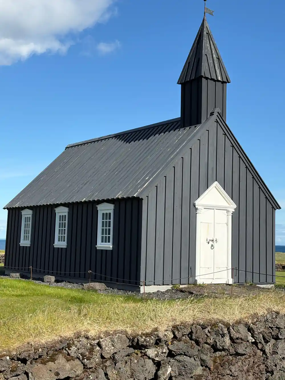 Black wooden church with white door and stone wall