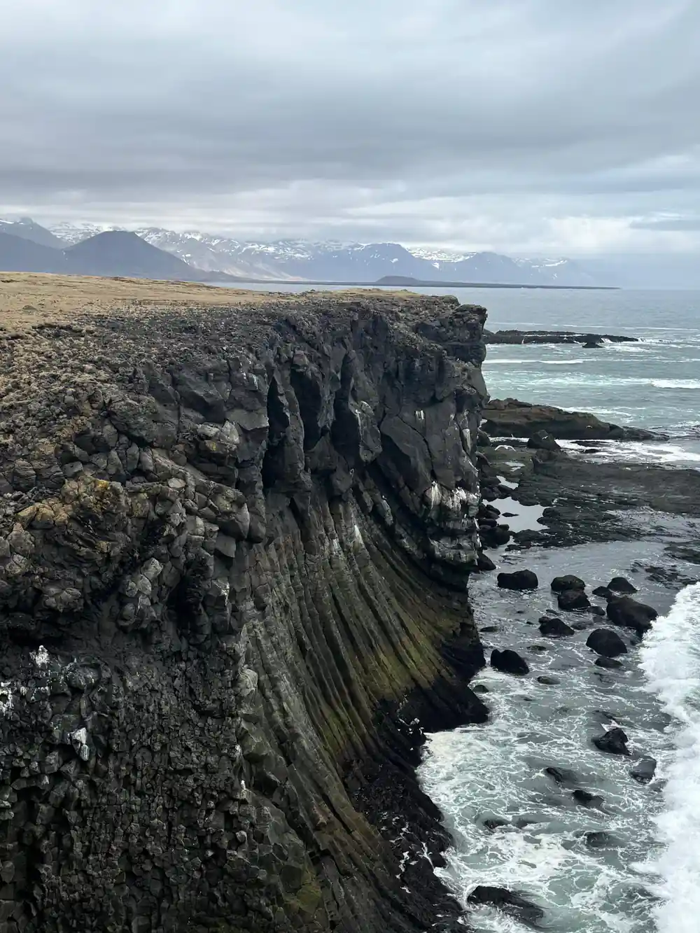 Columnar basalt cliff face meeting black sand beach and sea