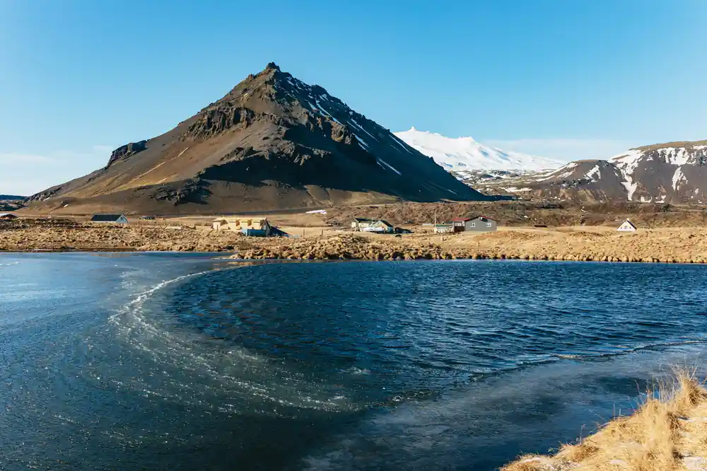 Cone mountain beside blue lake with snow patches