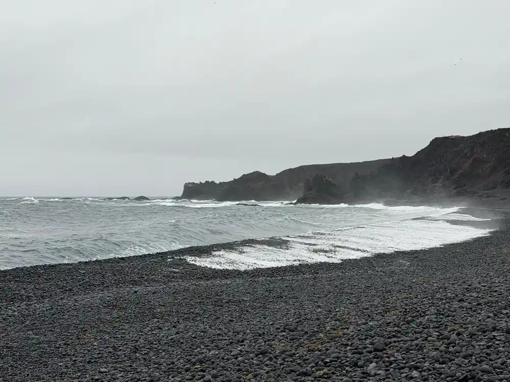 Dark sand beach with rocky cliffs and waves