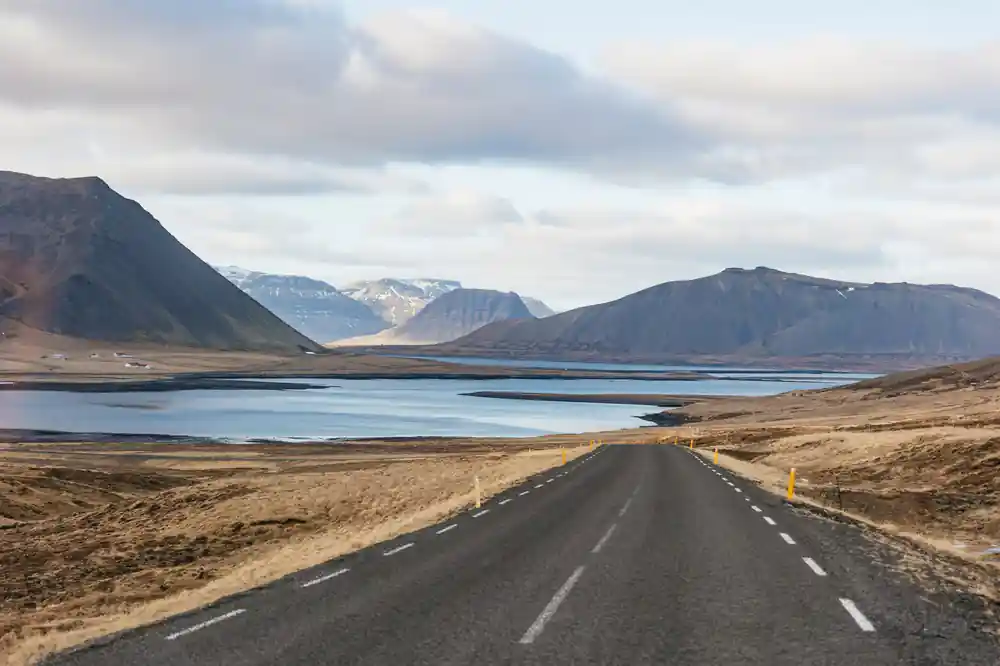 Empty road stretching toward mountains and lake landscape