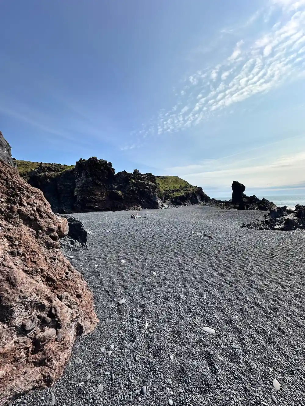 Grey pebble beach with rocky outcrops and distant hills