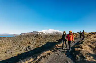 Group hiking on volcanic terrain with snow-capped mountain