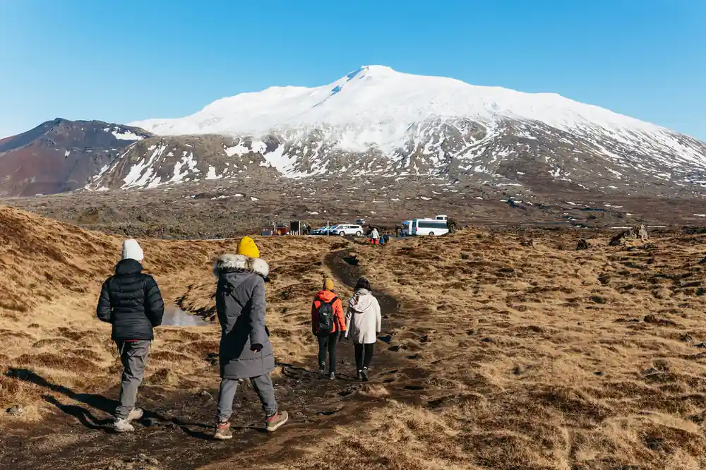 Group walking toward snow-capped mountain across tundra