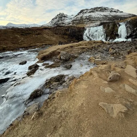 Kirkjufellsfoss waterfall half frozen below snowy mountains