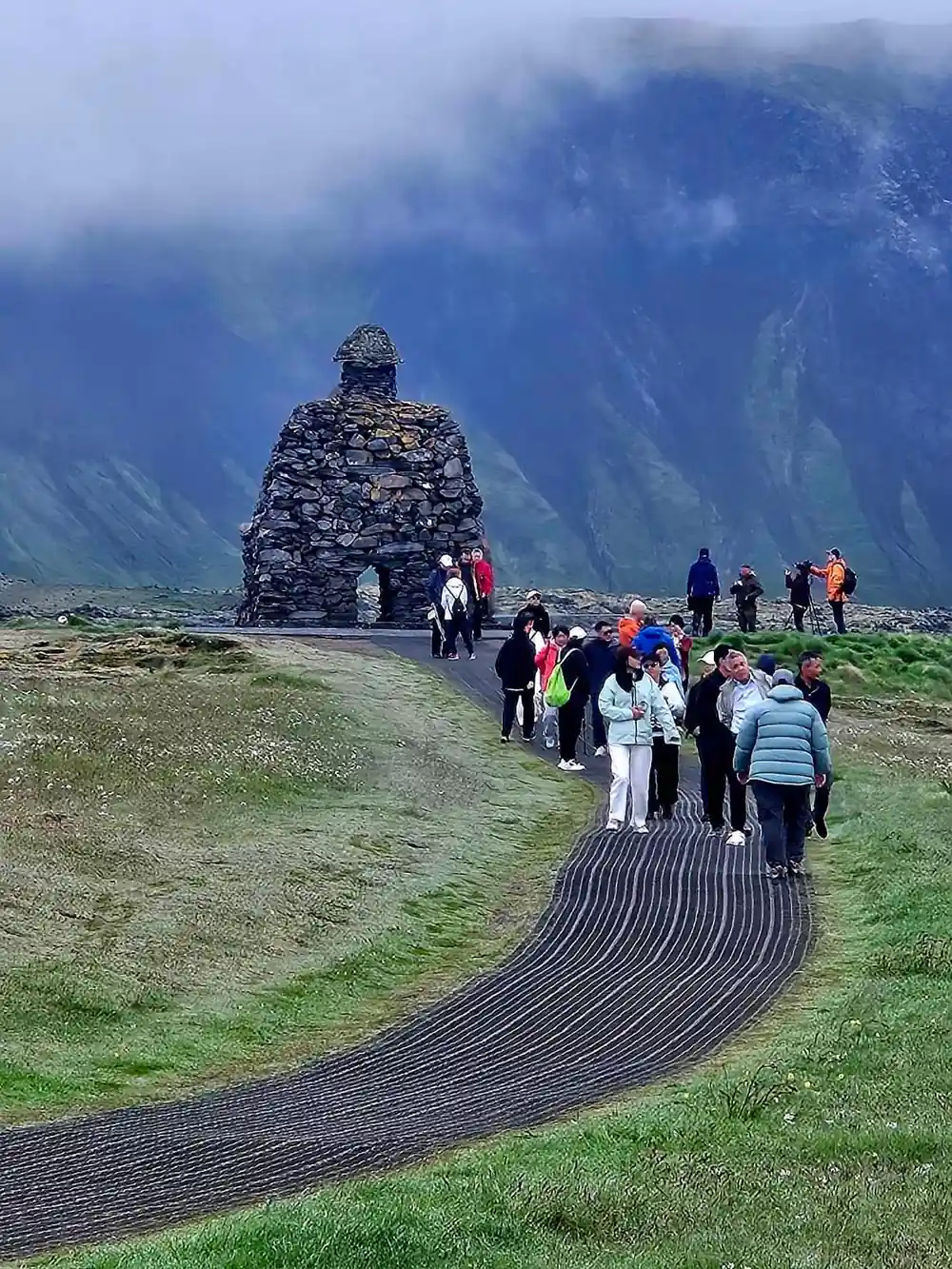 Tourists walking on dark road toward stacked stone cairn