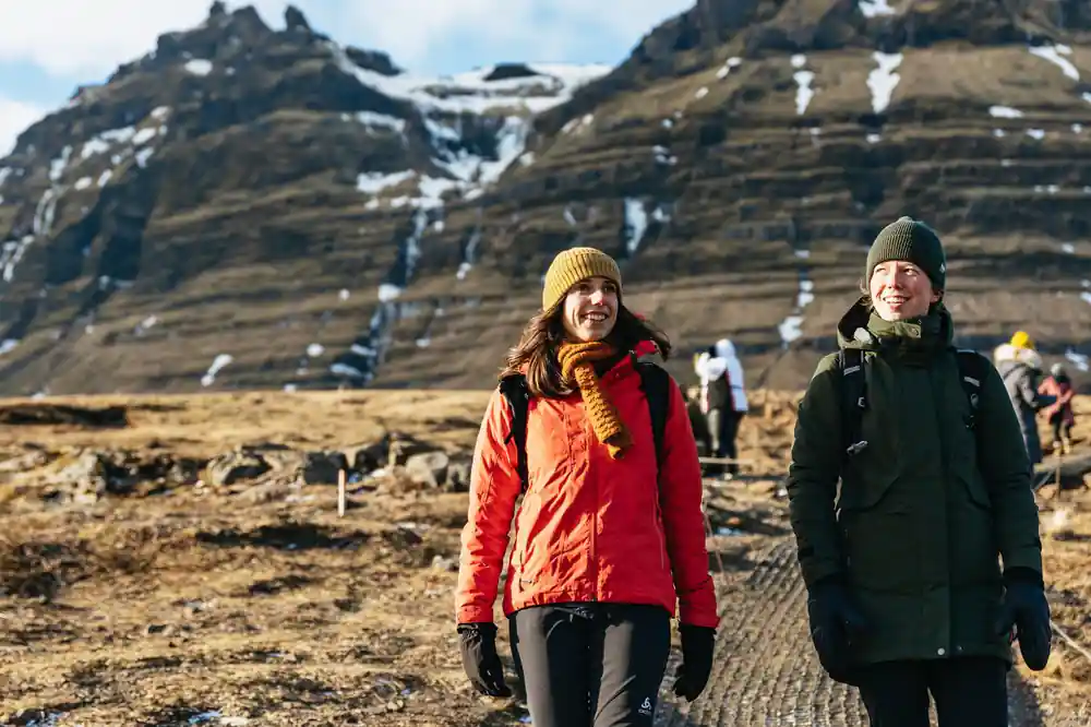 Two hikers in winter clothing on trail with snow mountain