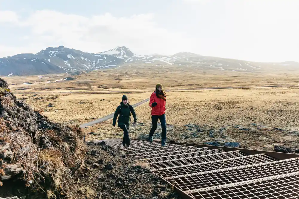 Two people on metal boardwalk in volcanic landscape with snow