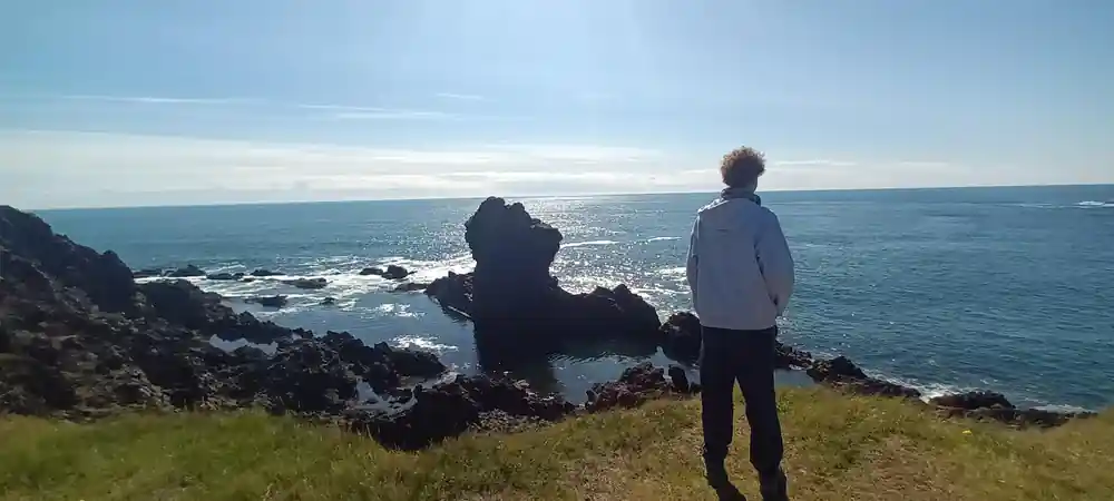 Two people standing on grassy cliff above rocky coastline