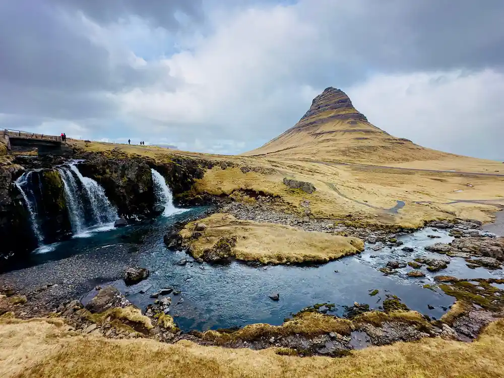 Waterfall cascading into pool below cone-shaped mountain