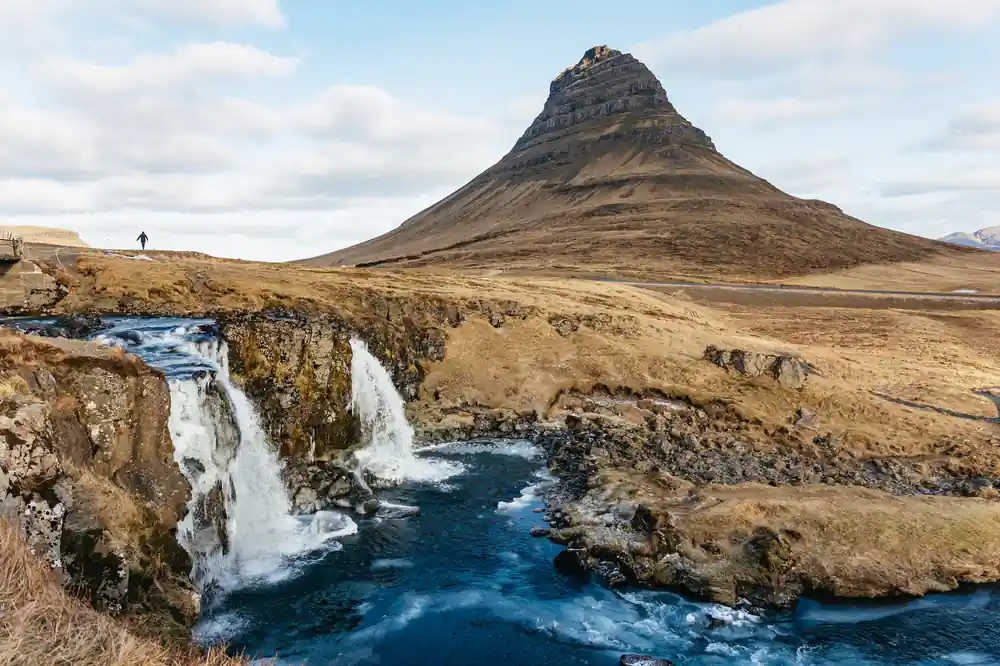 Waterfall flowing into blue river beneath distinctive mountain