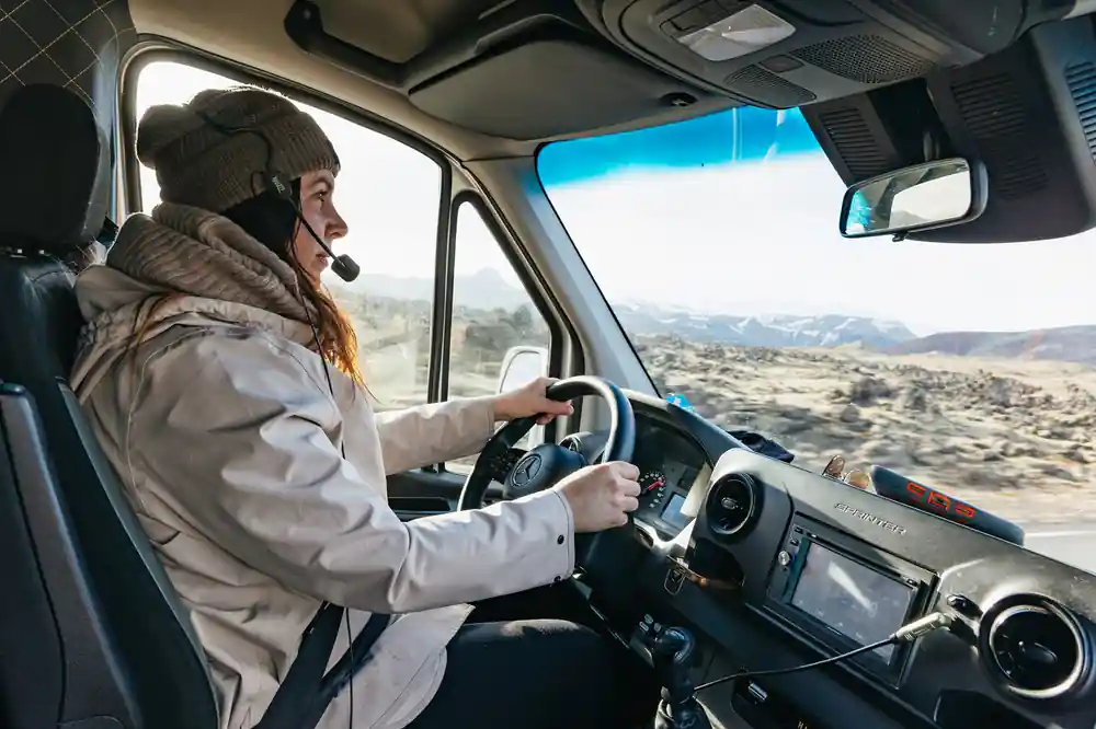 Woman driving minibus on mountain road with landscape