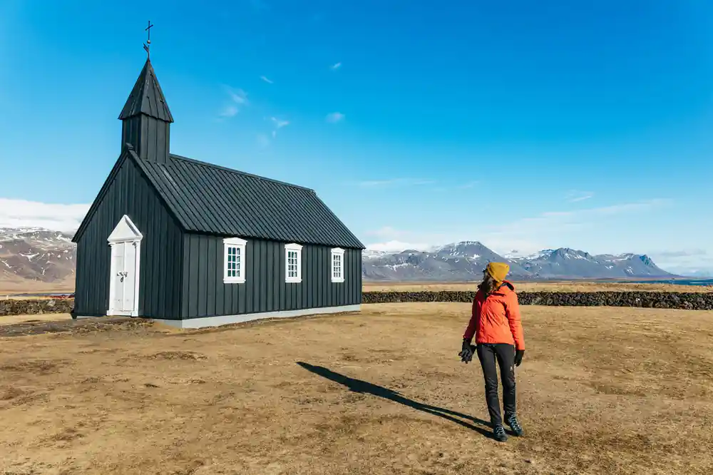 Woman in red jacket standing by black church in valley